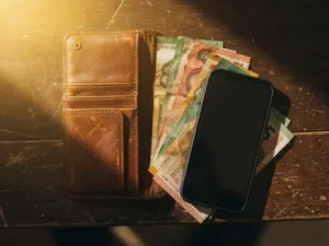 Worn leather wallet open on weathered wood with African banknotes, euro bills, and a smartphone in warm golden light.