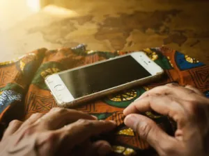 Worn iPhone on colorful African wax-print fabric over a wooden world map, warm hands adjusting settings in soft golden light.