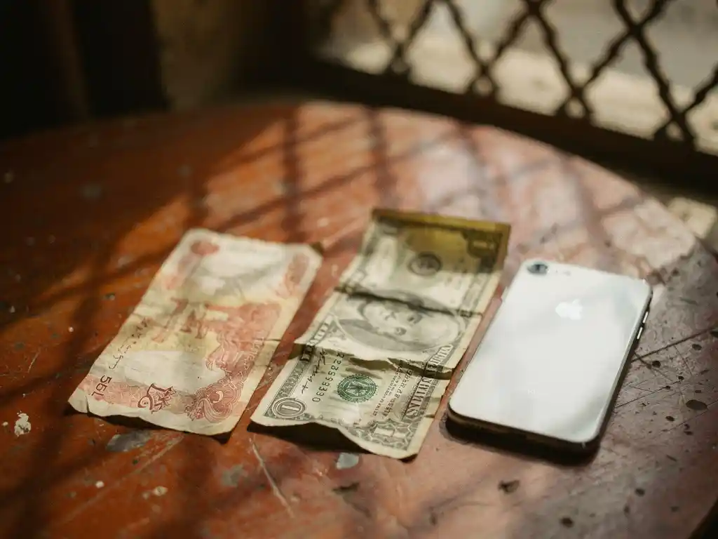 Worn Egyptian pound note and crumpled US dollar bill side by side on a weathered Cairo café table, soft afternoon light casting latticed shadows.