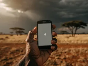 Weathered hand holding a basic mobile phone with one signal bar over an African savanna under stormy skies with acacia trees on the horizon.